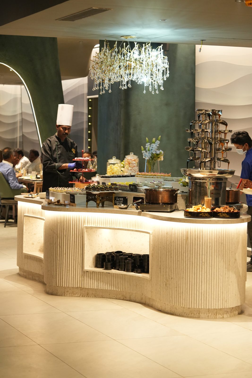 A curved marble buffet island lit from below, with a crystal chandelier above