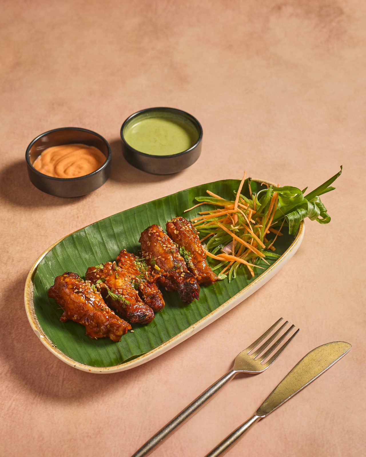 Glazed chicken wings on a banana leaf with carrot garnish and dips
