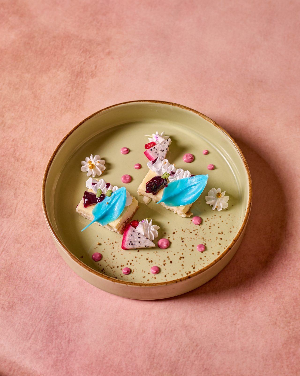 A plated dessert with blue and pink petal decorations on a pink background