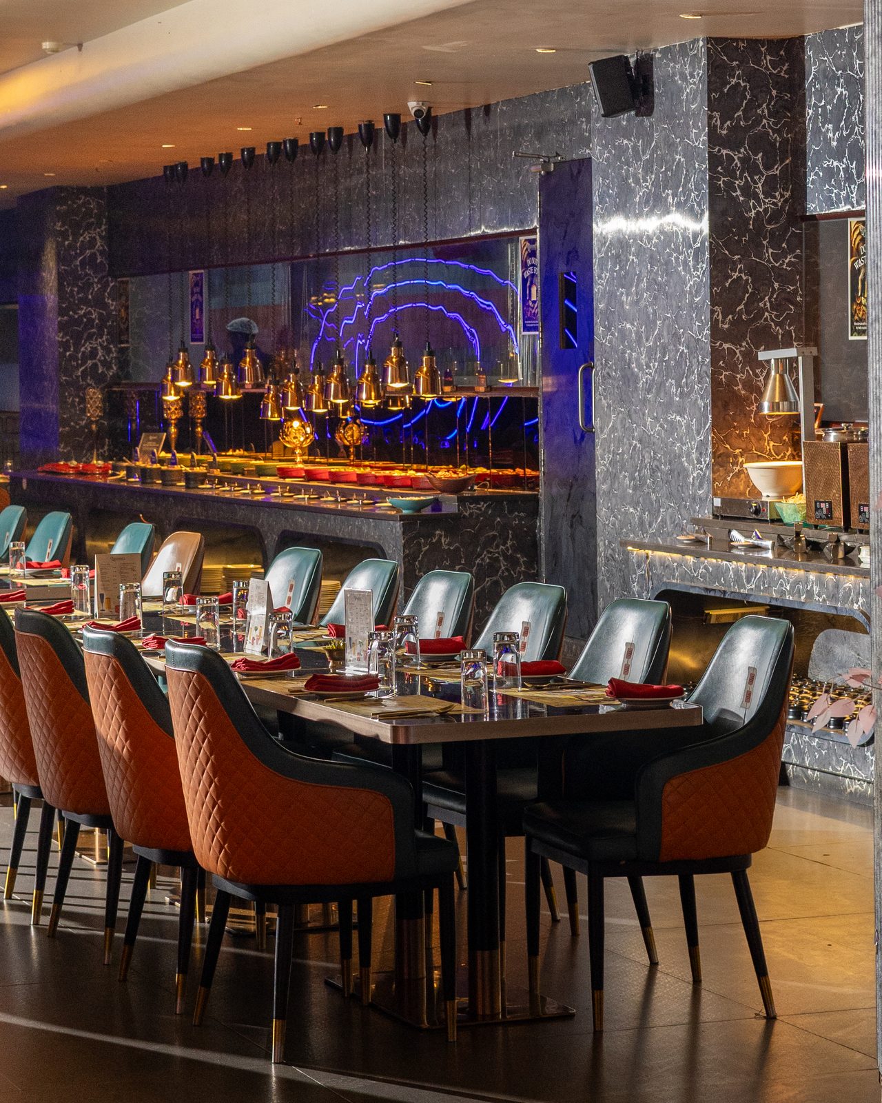 The dining hall with set tables and the live kitchen glowing behind