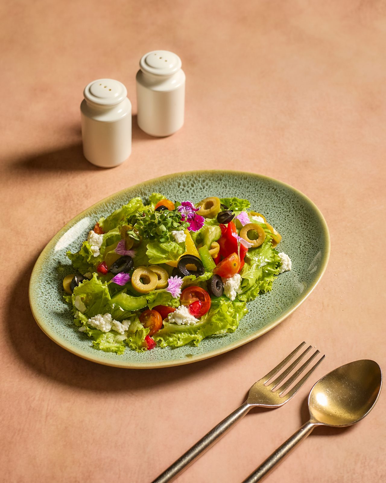 Fresh green salad with olives, tomatoes and feta on a pale green plate