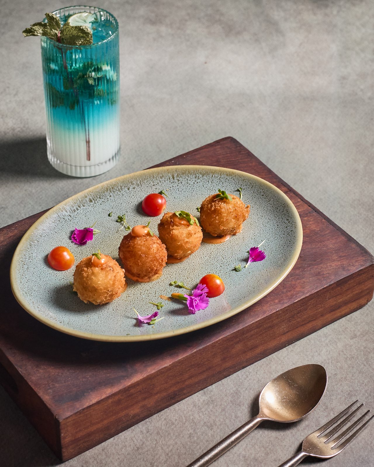 Crispy golden croquettes on a stoneware plate beside a blue mocktail